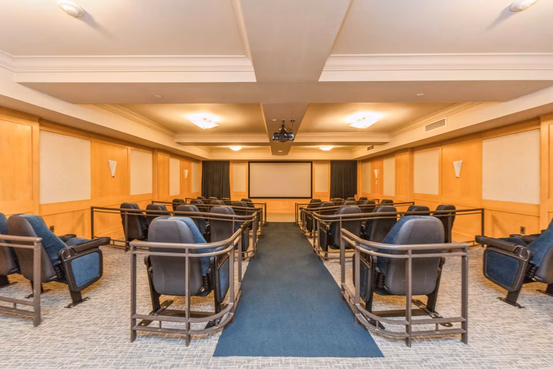 A small theater-style media room with rows of blue reclining seats facing a projection screen.