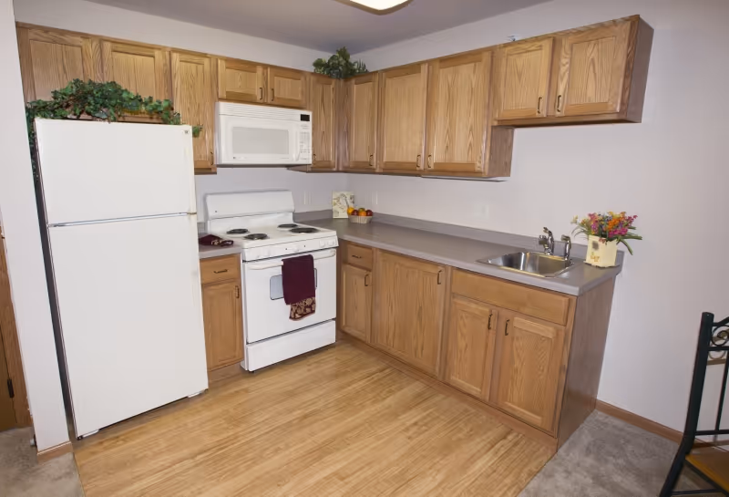 Compact kitchen with oak cabinets, a white refrigerator, stove and microwave, a countertop sink, and wood-look flooring.