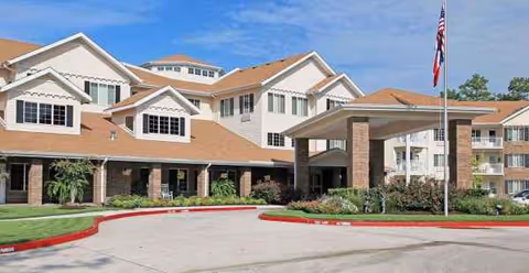 Exterior view of Cypress Woods Sky Active Living with entrance canopy and flag.