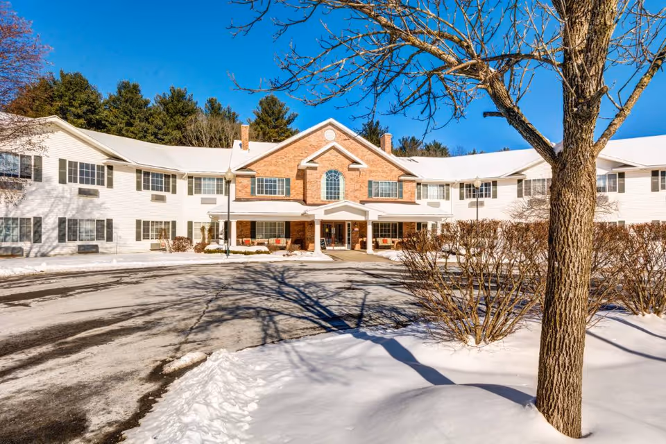 Front exterior of a two-story building with a central brick entrance, snow-covered grounds, and a large leafless tree in the foreground.
