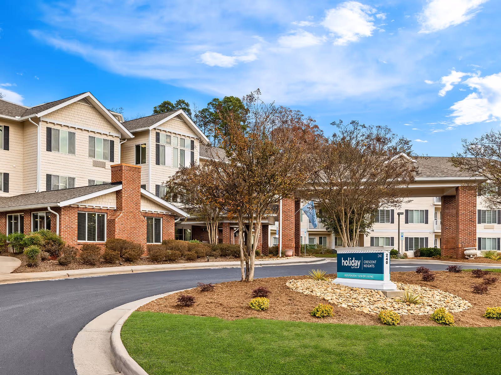 Exterior view of Holiday Crescent Heights facility with brick columns, driveway, and landscaped front yard.