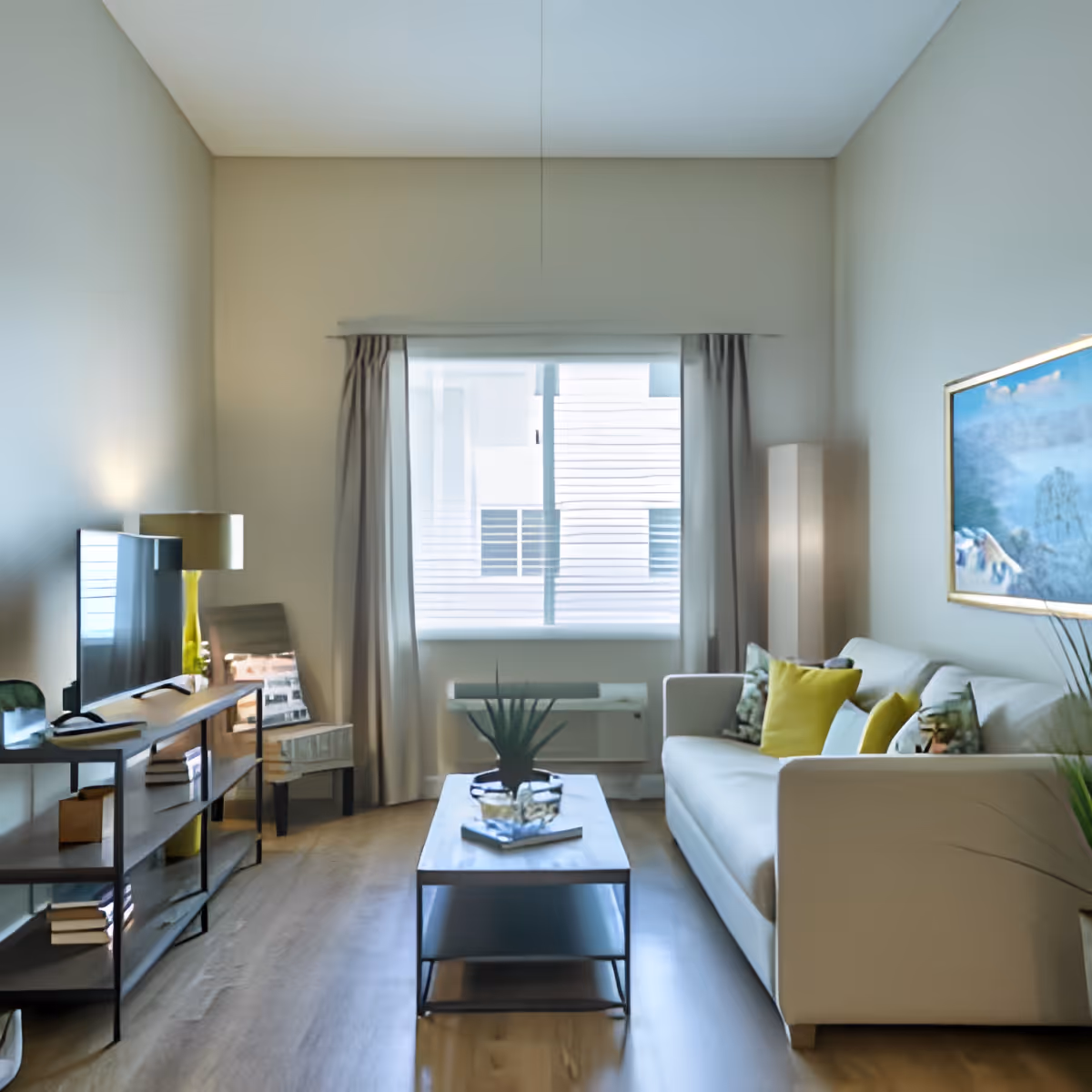 A modern living room with a white sofa adorned with green and yellow pillows, a wooden coffee table with a plant and books, a flat-screen TV on a wooden stand, a floor lamp, a chair, and a large window with curtains letting in natural light.