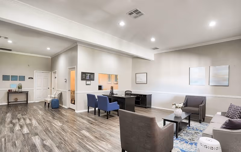 Spacious modern reception lounge with a front desk, several chairs and sofas, artwork on light walls, and wood-look flooring.