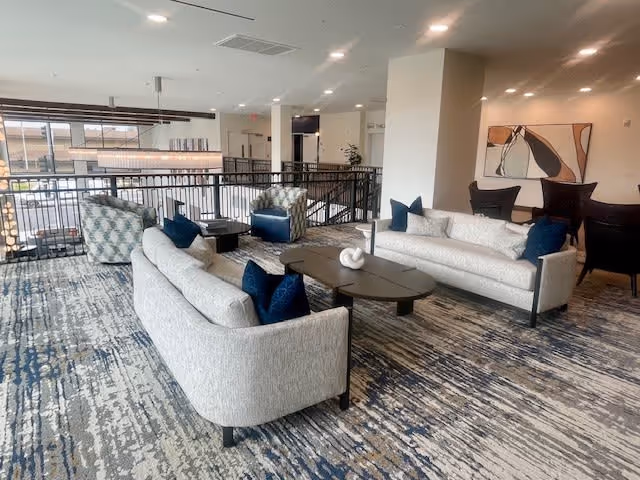 Open interior lounge with two curved sofas, armchairs, and coffee tables on a patterned carpet overlooking a railing.