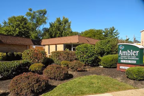 Exterior view of Ambler Extended Care Center with landscaped shrubs and a sign.