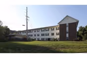 Two-story senior living facility with white siding and brick accents sits on a grassy front lawn.