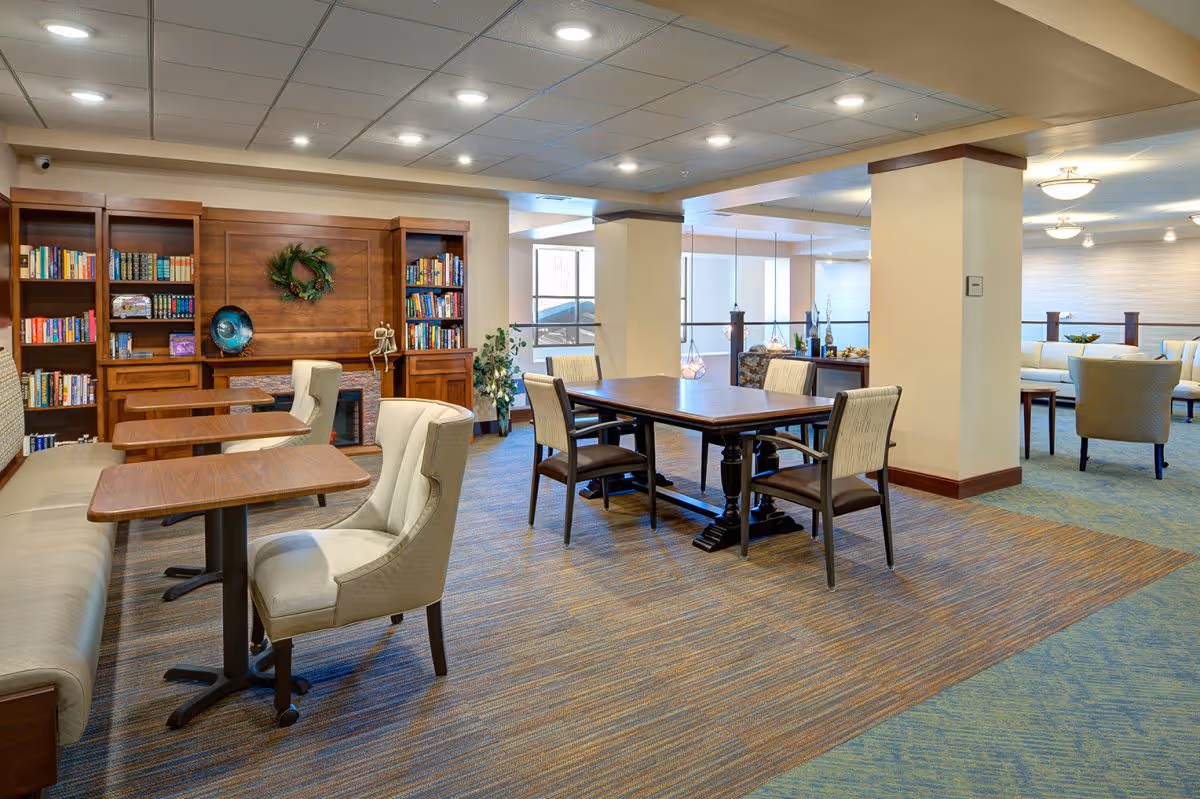 Open communal dining and lounge area with tables, chairs, bookshelves, and soft seating.