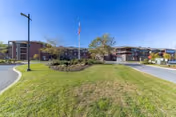 Front exterior of The Summit senior living building with a flagpole, landscaped lawn, and a circular driveway beneath a clear blue sky.