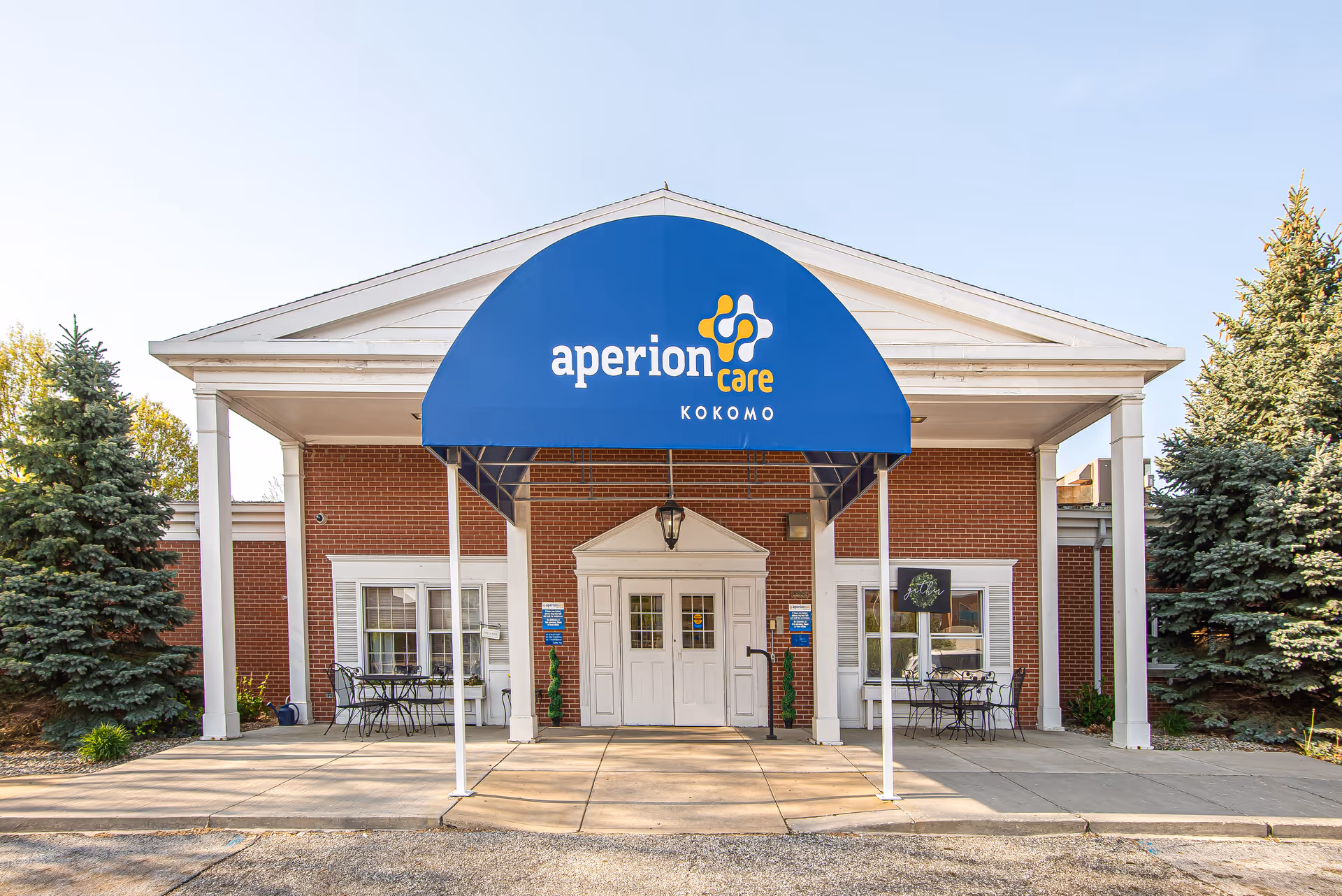 Front entrance of Aperion Care Kokomo with a blue awning over double doors and a brick facade.