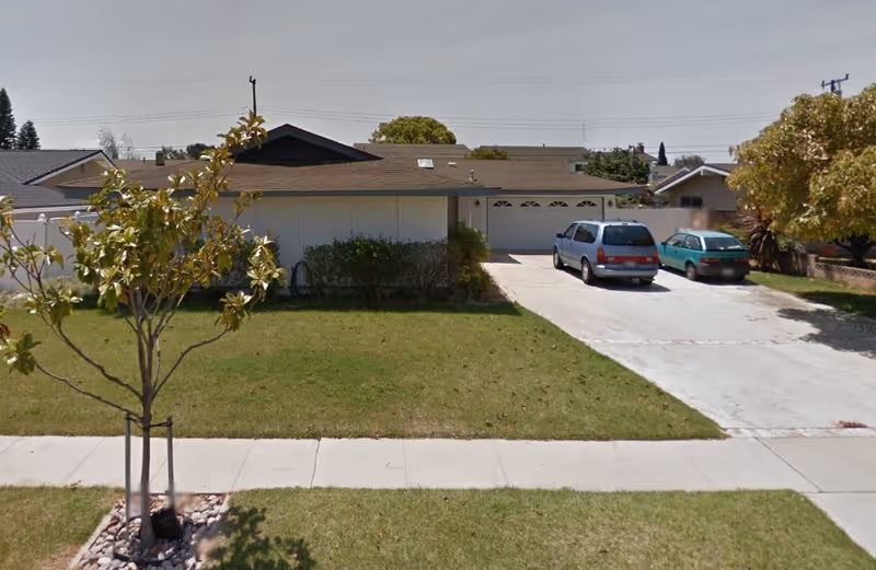Single-story suburban house front with a lawn, driveway, and two cars parked in front of a garage.