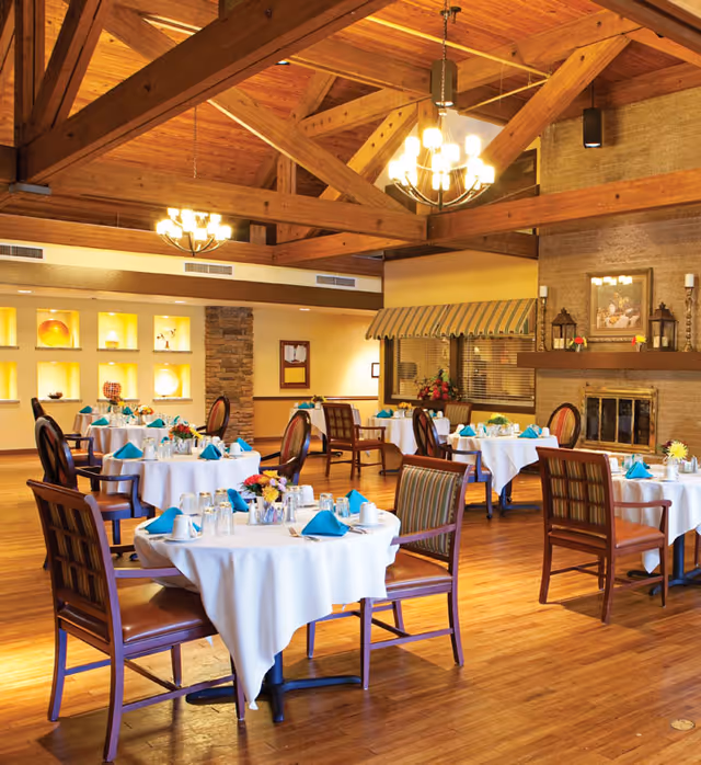 Dining room with round tables dressed in white linens and teal napkins beneath exposed wooden beams and chandeliers.