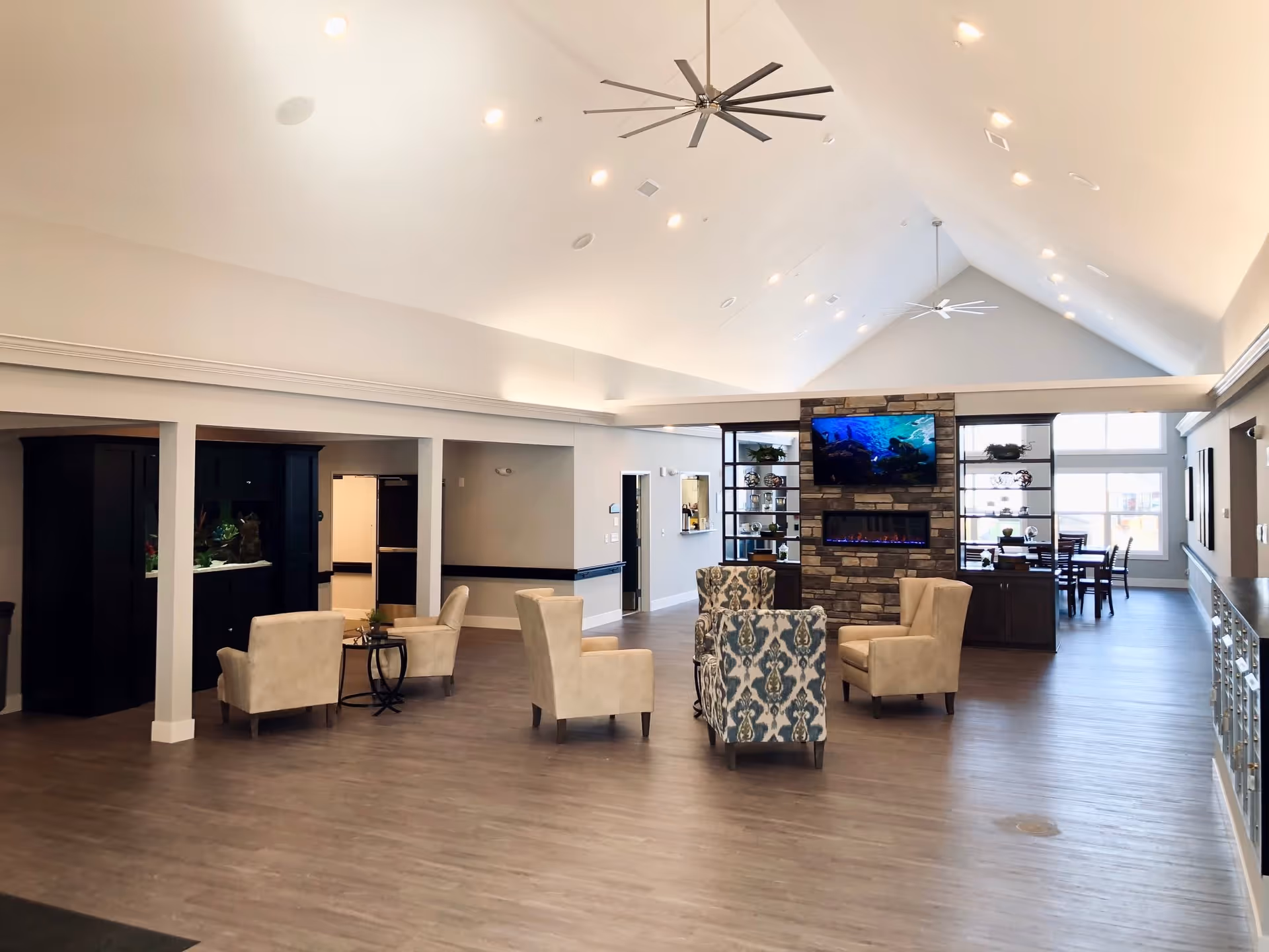 Spacious vaulted communal lounge with seating, a stone fireplace and TV, and a dining area visible in the background.