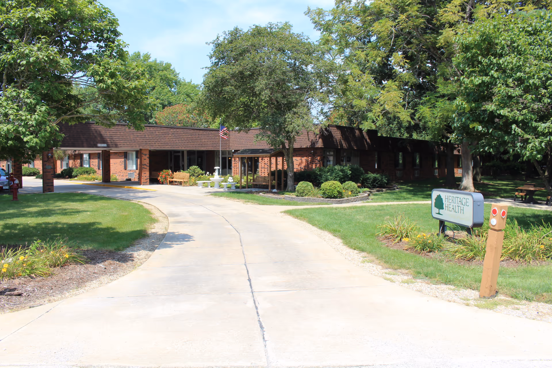 Driveway leading to the front entrance of a single-story brick health facility with trees, lawn, and a 'Heritage Health' sign.