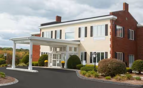 Exterior view of a two-story senior living facility with a covered entrance and landscaped driveway.