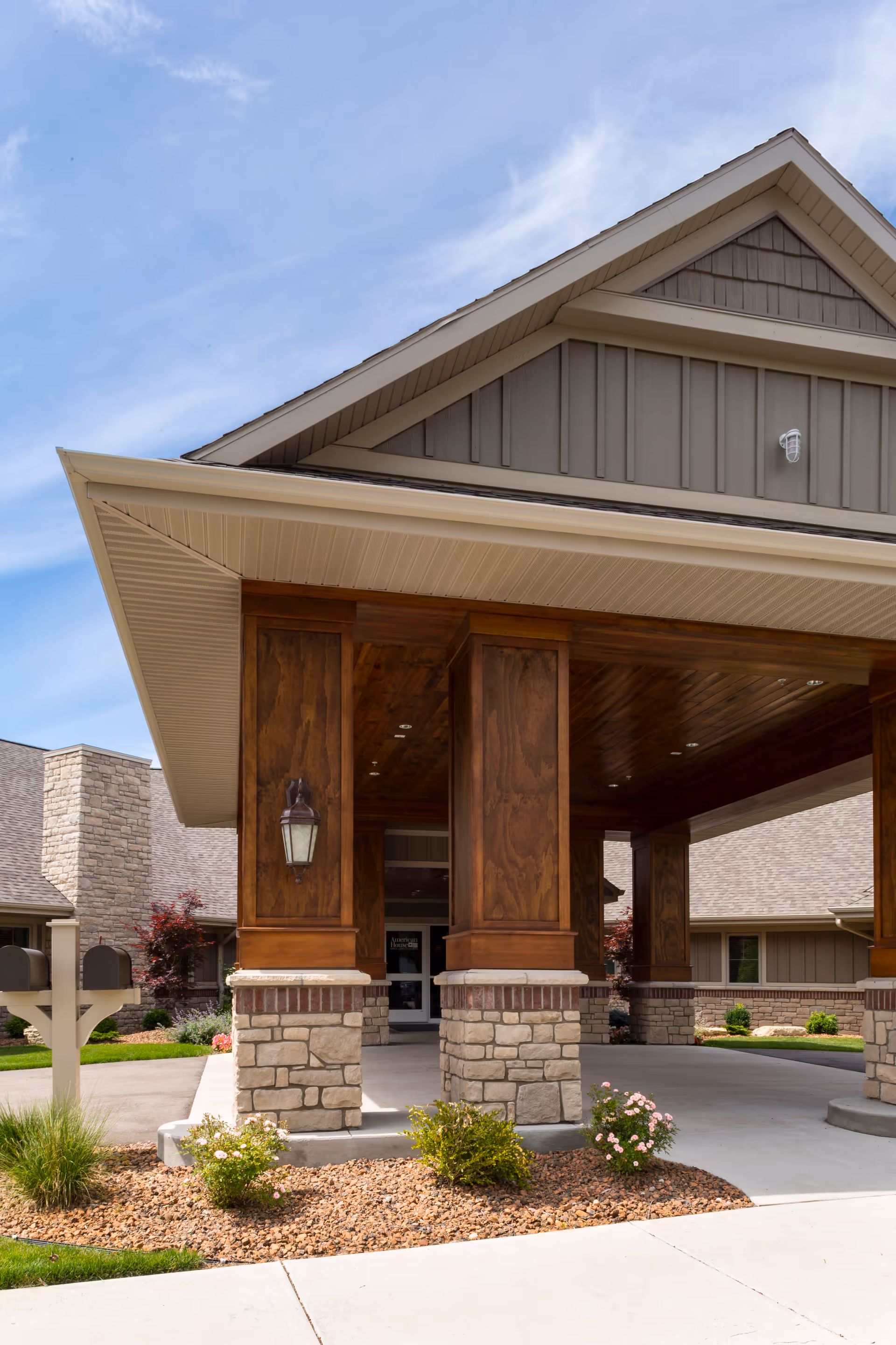 Covered entrance portico of a senior living building with large wooden columns on stone bases and a landscaped driveway.