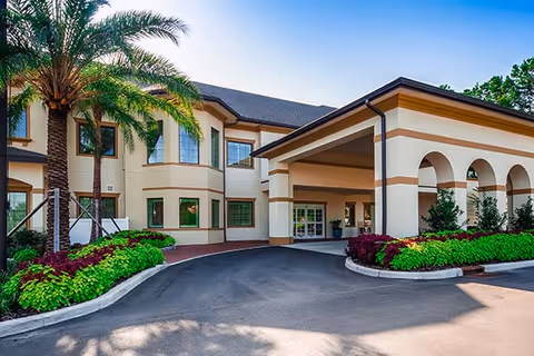 Front view of The Windsor of Gainesville, a beige senior living facility with arches and landscaping.