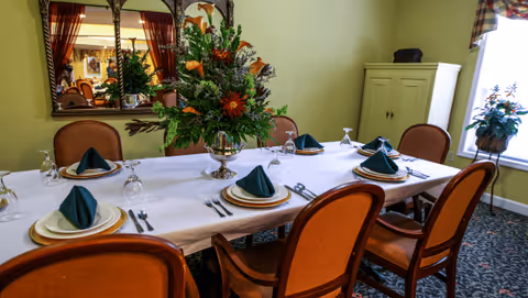 A formal dining table set with plates, folded green napkins, glassware, and a large floral centerpiece in a decorated room.