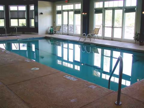 Indoor pool area with ladders, rails, and bright windows reflecting on water.