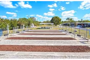 Multiple empty mobile home/RV pads with gravel and utility hookups under a blue sky at Buccaneer Mobile Estates.