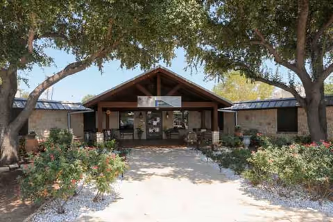 Front entrance of Lake Village Nursing and Rehabilitation Center with trees and landscaping.