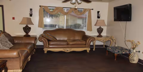 Cozy living room with brown leather sofas, lamps, and a wall-mounted TV.
