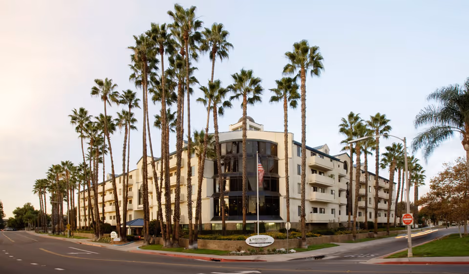 Front exterior of the multi-story Westmont of Escondido building flanked by tall palm trees along a street.