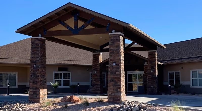 Covered front entrance with timber roof and stone columns at the front of a single-story building under a clear blue sky.
