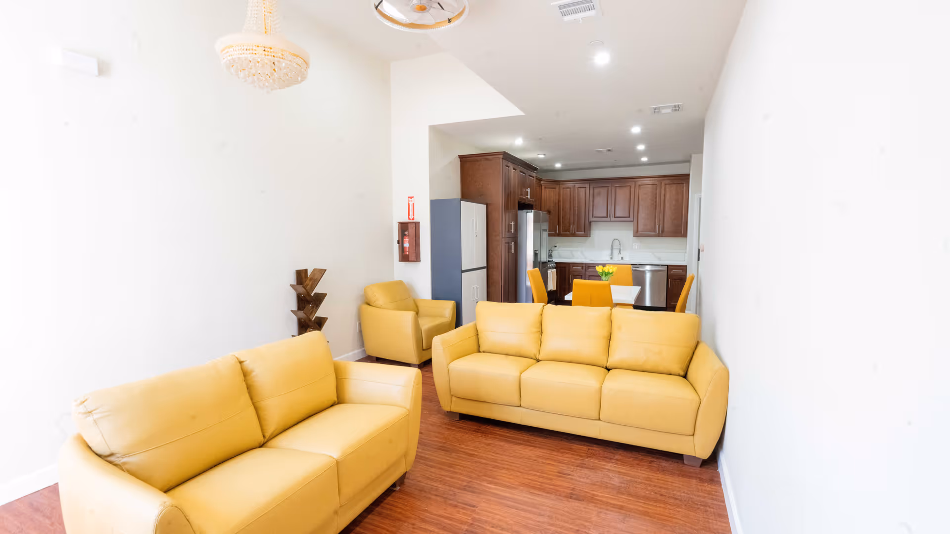 Open-plan living area with yellow sofas and chairs and a kitchen with wooden cabinets in the background.
