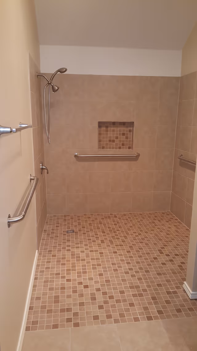 Accessible tiled shower with grab bars, mosaic niche, and level entry.