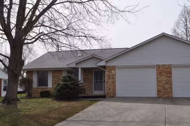 Single-story brick house with an attached two-car garage, driveway, and leafless trees in front.