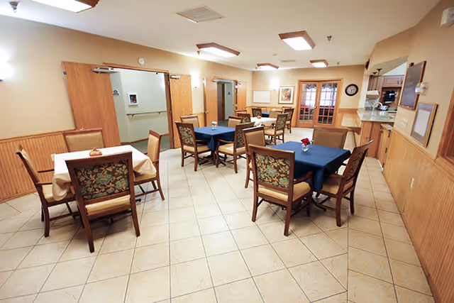 Communal dining room with several tables and chairs, tiled floor, and a serving counter.