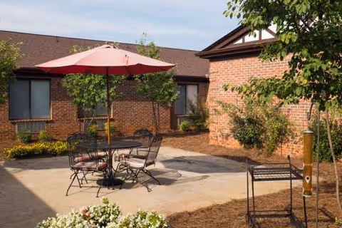 Outdoor courtyard with a table, chairs, umbrella, and brick building facade.