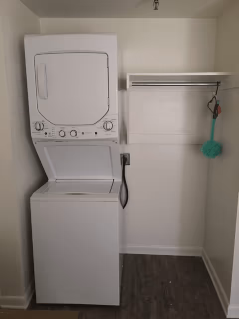Stacked washer and dryer in a small laundry closet with a shelf and hanging rod.