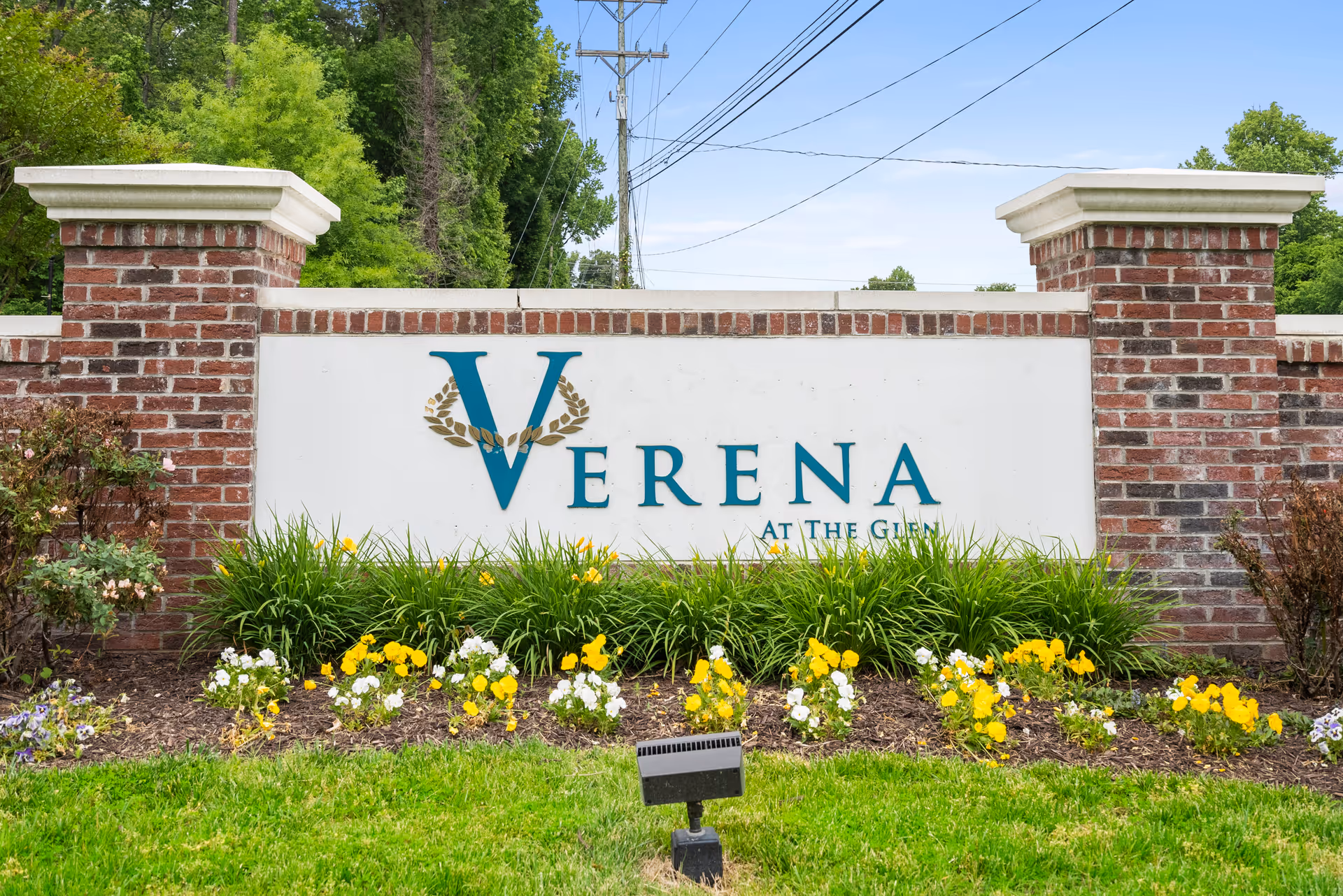 Brick entrance sign reading "Verena at the Glen" with landscaping and yellow flowers in front.