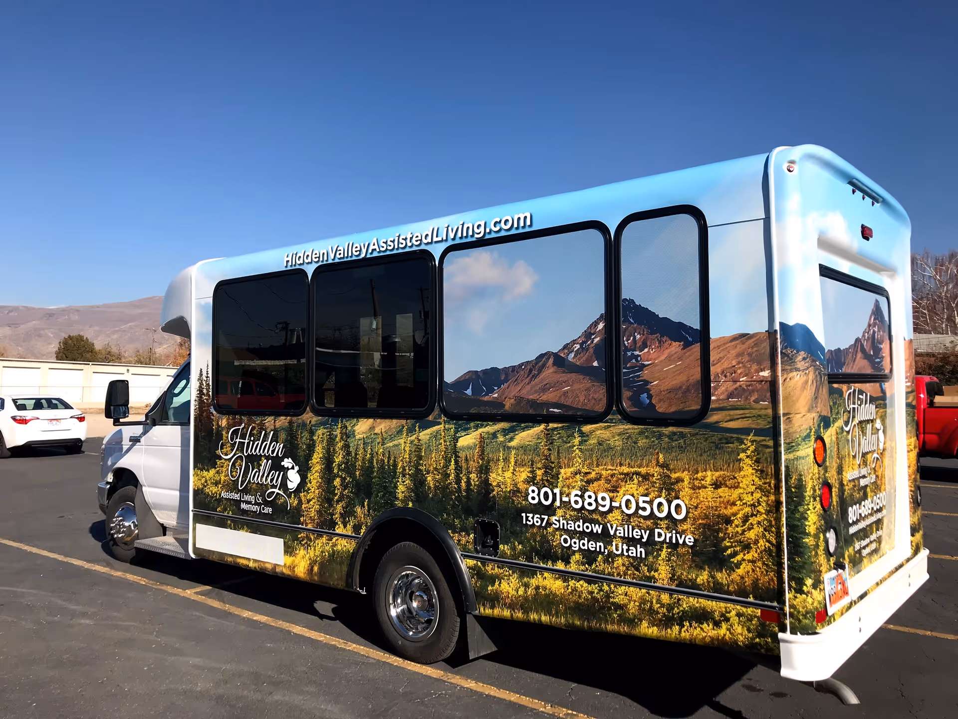 A shuttle bus wrapped with mountain and valley graphics advertising Hidden Valley Assisted Living and Memory Care parked in a parking lot.