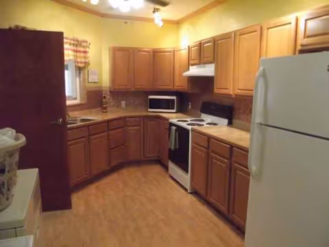 U-shaped wooden kitchen in Five Oaks Rehabilitation and Care Center with fridge, stove, and cabinets.