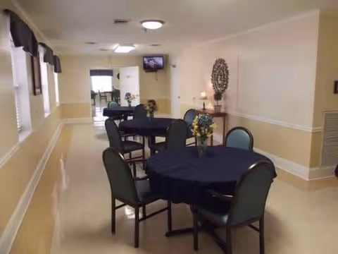 Empty dining area with round tables, dark tablecloths, and chairs in a hallway-like room.