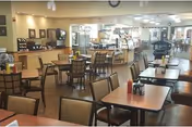 Spacious dining area with multiple tables and chairs and a self-service counter and food display in the background.