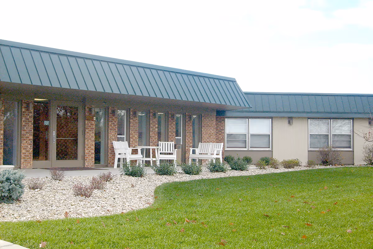Exterior view of Tallgrass Healthcare Campus with a brick building, metal roof, and white outdoor seating along the entrance.