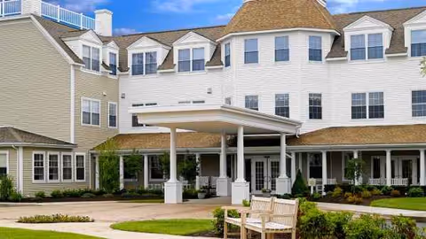 Exterior view of Atria Aquidneck Place with a covered entrance and bench.