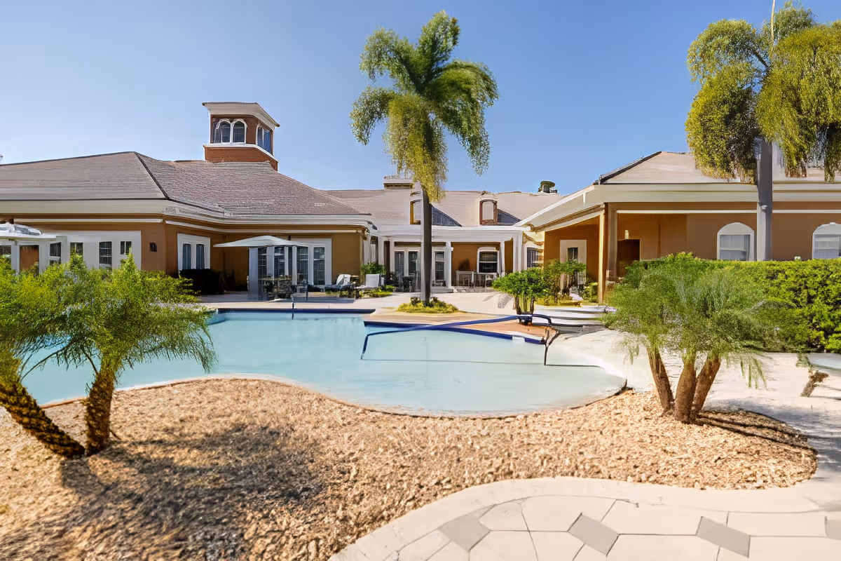 Courtyard with a swimming pool, palm trees, and a single-story senior living building in the background.