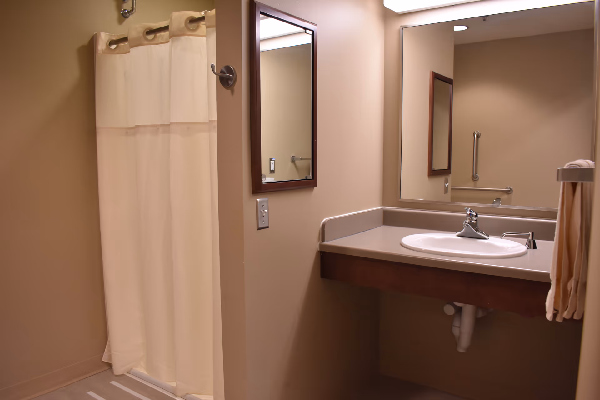 Accessible bathroom with a sink and counter beneath a large mirror and a curtained shower stall.