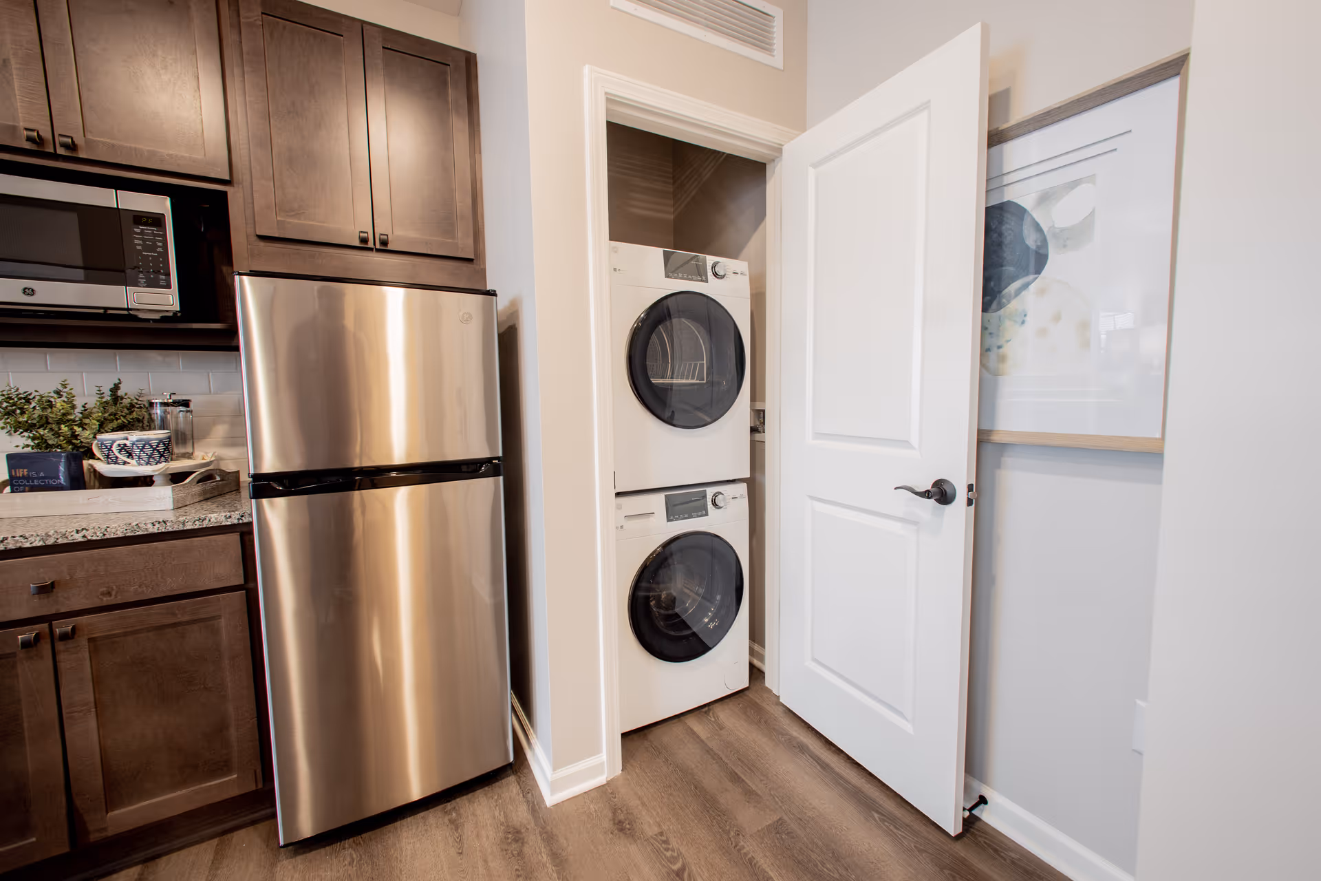 Small kitchen area with a stainless steel refrigerator and a closet containing a stacked washer and dryer behind an open white door.