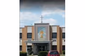 Front exterior view of Misericordia Nursing & Rehabilitation Center building with a large religious image and a cross above the entrance, under a partly cloudy sky. A red vehicle is parked in front of the entrance.