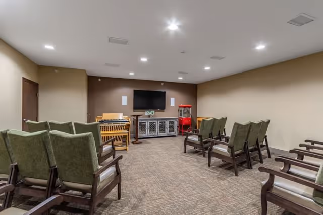 Small media room with rows of upholstered chairs facing a wall-mounted TV, a cabinet, and a popcorn machine.