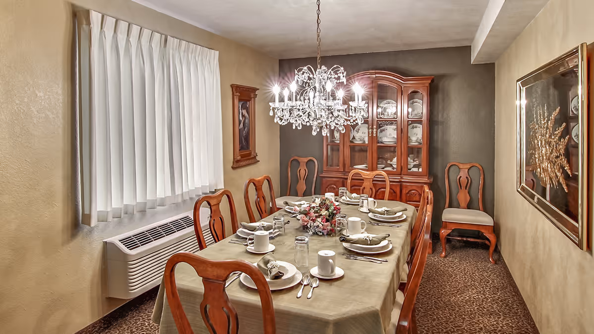 Formal dining room with a long set table, wooden chairs, a crystal chandelier, and a china cabinet.