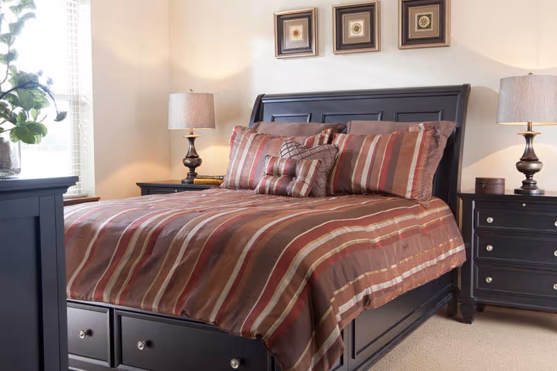 A neatly made bedroom with a dark wood bed dressed in striped brown bedding, flanked by matching nightstands and lamps.