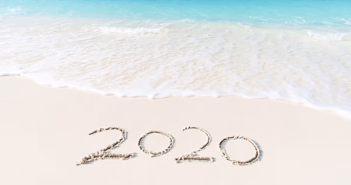 Turquoise ocean waves washing onto a sandy beach with "2020" written in the sand.