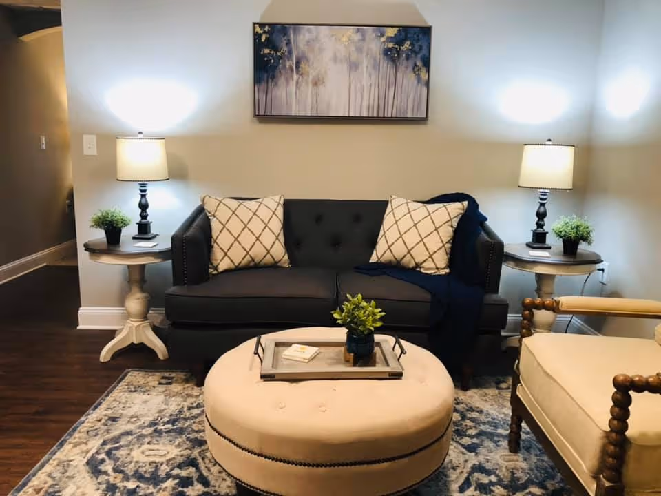 Cozy living room with a dark gray tufted sofa between two side tables with lamps, a round beige ottoman coffee table, and an accent chair.