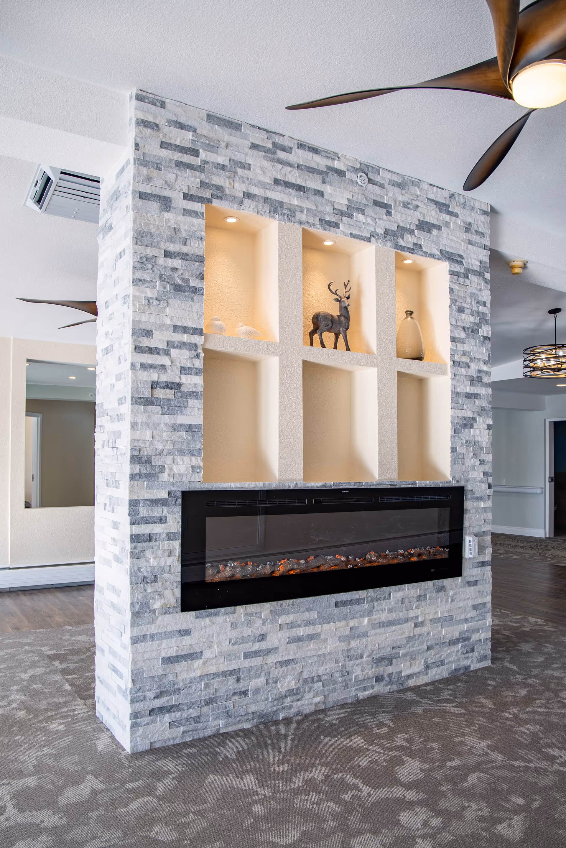 A stone-clad interior partition with a built-in electric fireplace and illuminated display niches holding decorative items in a lounge.